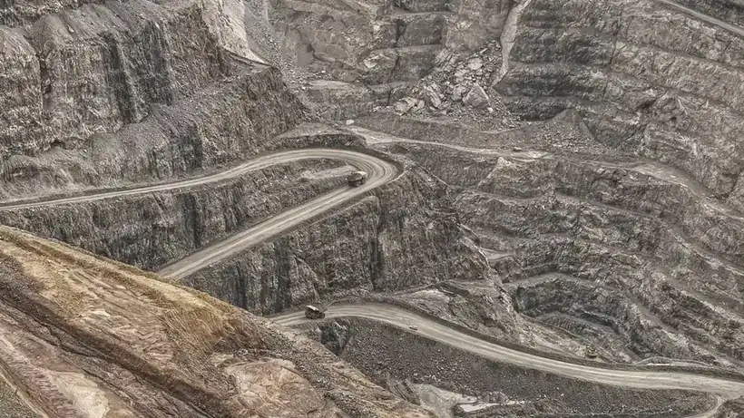 Cava a céu aberto em bancadas sucessivas, com a estrada de serviço em ziguezague pelas faces